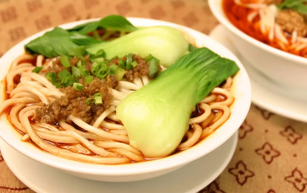 A steaming bowl of Dan Dan noodles in rich Sweet-Spicy Sauce, crowned with minced pork, crushed peanuts, and a ribbon of Hot Honey Diablo Sauce.